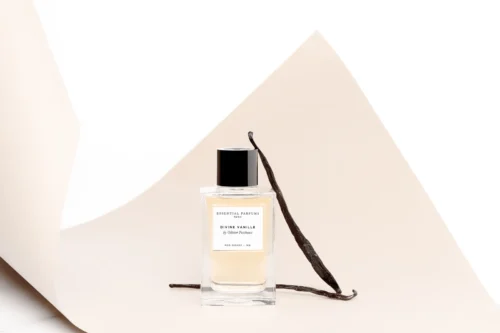 Frasco de Divine Vanille apoyado en un fondo de papel curvado color crema, con dos vainas de vainilla junto al frasco