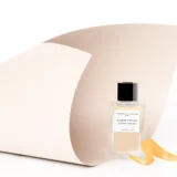 Frasco de Orange X Santal 100 ml junto a piel de naranja en una composición de estudio.