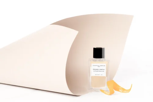 Essential Parfums Orange X Santal 100ml - Ambient Frasco de Orange X Santal 100 ml junto a piel de naranja en una composición de estudio.