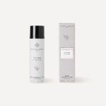 Botella de producto cosmético con tapa negra y caja de cartón gris, ideal para el cuidado de la piel.