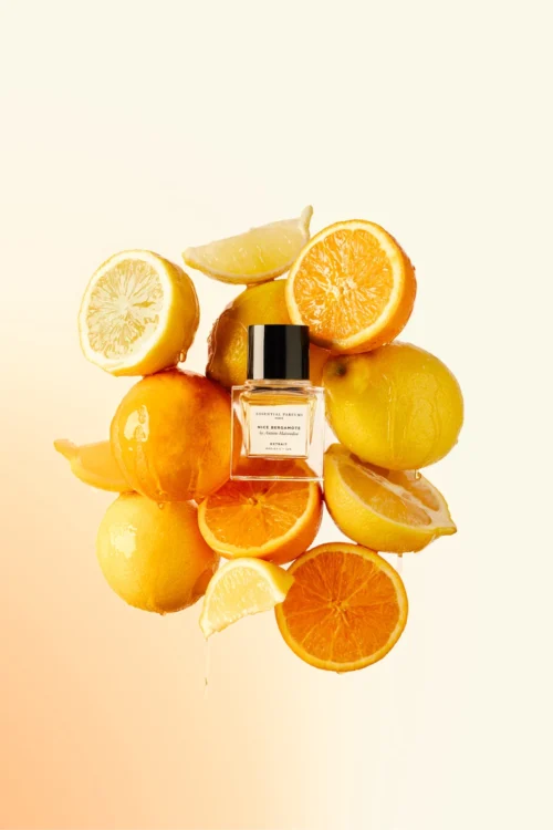 Essential Parfums Nice Bergamote Extrait 30 ml - Ambiente Frasco de Nice Bergamote Extrait entre limones y naranjas partidos y chorreantes sobre fondo degradado en tonos crema y naranja